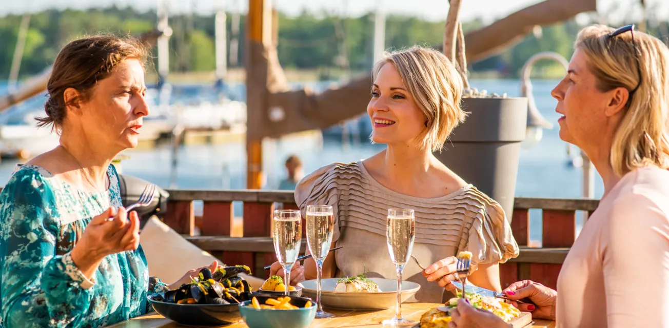 Kvinnor äter middag i kvällssolen vid restaurang ÅSS Paviljongen i Mariehamns västra hamn.