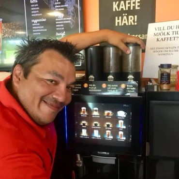 Medarbetare bredvid kaffeautomaten, som erbjuder olika sorters kaffe.