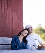 Par som sitter och fikar framför röd stuga.