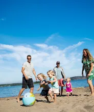 Barn och vuxna som leker med en badboll på sandstranden vid Lilla Holmen.