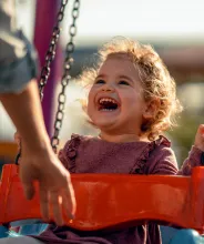 Glad liten flicka har roligt i en gunga på en lekpark.