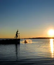 Person som hoppar i vattnet från badbrygga i solnedgången.