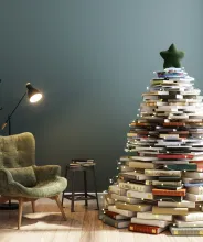 Julgran i form av böcker i ett vardagsrum med läsfotölj och lampa.