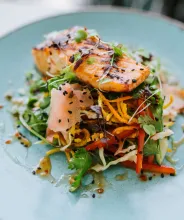 Gourmettallrik med grillad lax, inlagda och färska grönsaker och topping på en ljusblå tallrik.