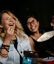 Unga kvinnor med popcorn skrattar på bio.