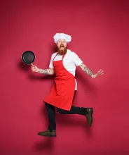 Kock med stekpanna och rött förkläde gör ett roligt hopp.