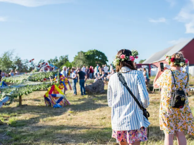 Kvinna fotograferar lövning av stången vid midsommarfirande på Bergö.