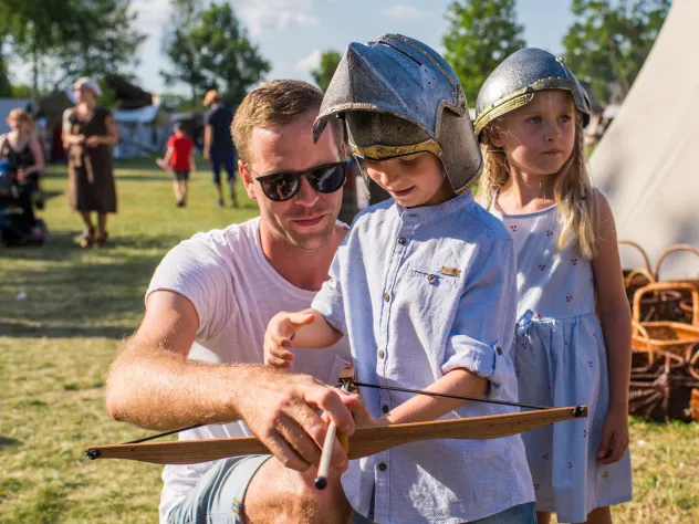 Barn med förälder spänner pilbåge på Vikingamarknaden i Kvarnbo.