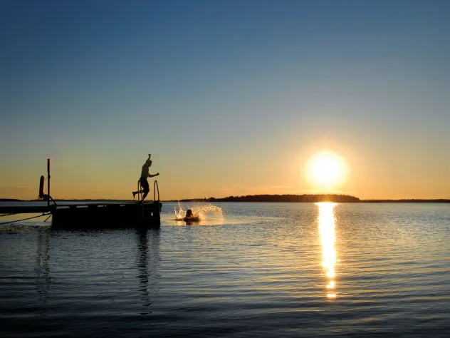 Person som hoppar i vattnet från badbrygga i solnedgången.