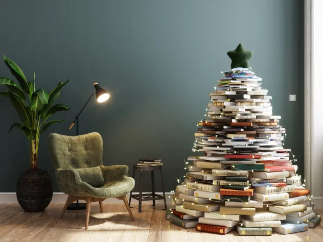 Julgran i form av böcker i ett vardagsrum med läsfotölj och lampa.