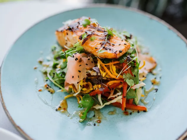 Gourmettallrik med grillad lax, inlagda och färska grönsaker och topping på en ljusblå tallrik.