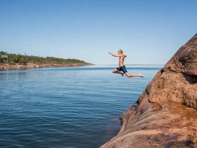 Pojke hoppar i vattnet från badklippa på Åland.