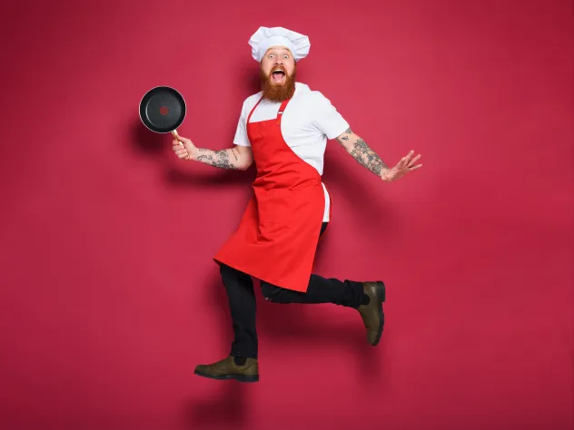 Kock med stekpanna och rött förkläde gör ett roligt hopp.