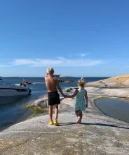 Pojke och flicka går hand i hand över klipporna på en ö i den åländska skärgården.