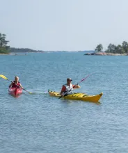 Två personer i varsin kajak som paddlar i Ålands skärgård.