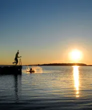 Person som hoppar i vattnet från badbrygga i solnedgången.