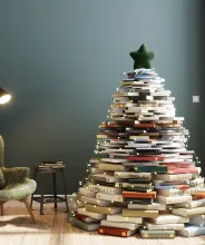 Julgran i form av böcker i ett vardagsrum med läsfotölj och lampa.