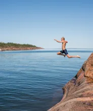 Pojke hoppar i vattnet från badklippa på Åland.