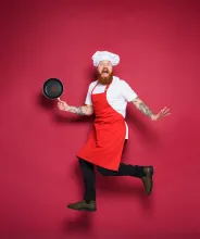 Kock med stekpanna och rött förkläde gör ett roligt hopp.