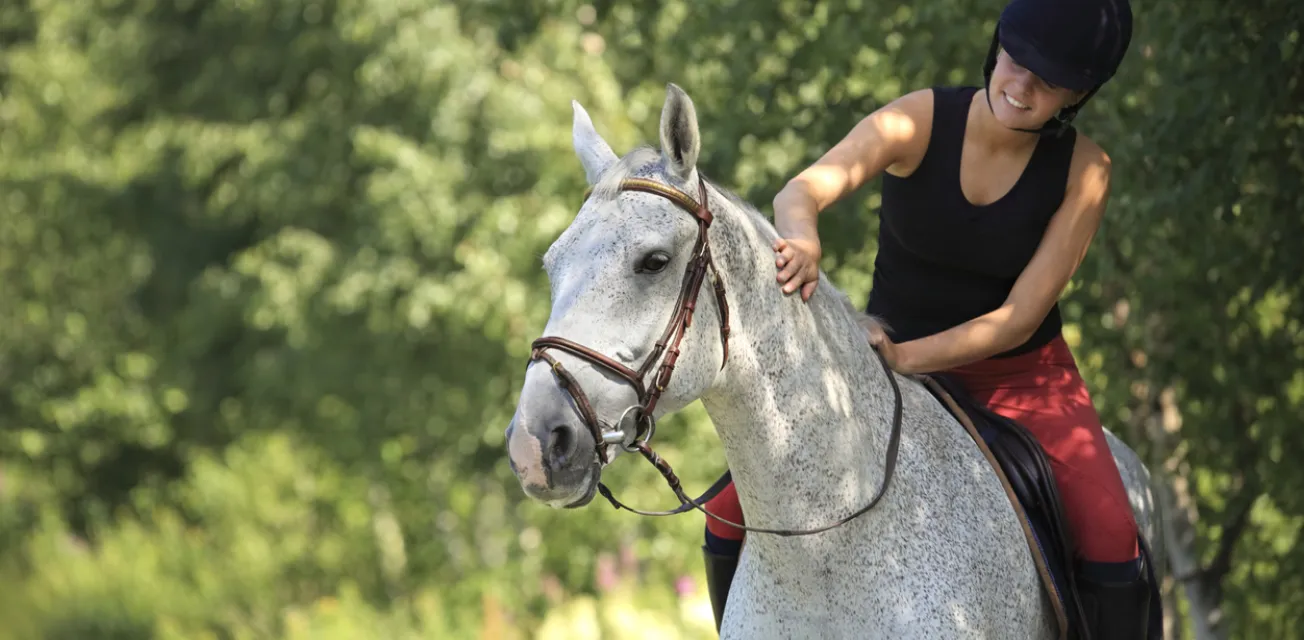 Kvinna som rider på en vit häst i skogen på sommaren.