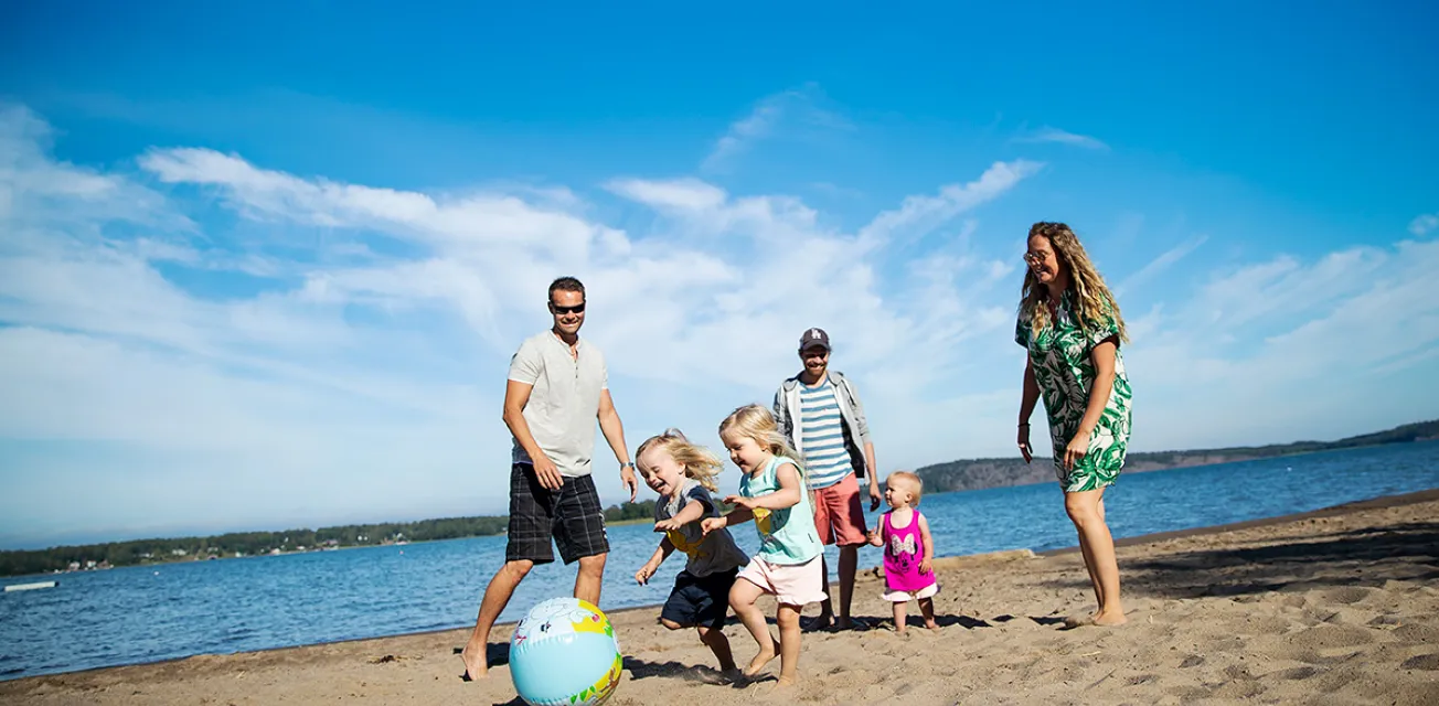 Barn och vuxna som leker med en badboll på sandstranden vid Lilla Holmen.