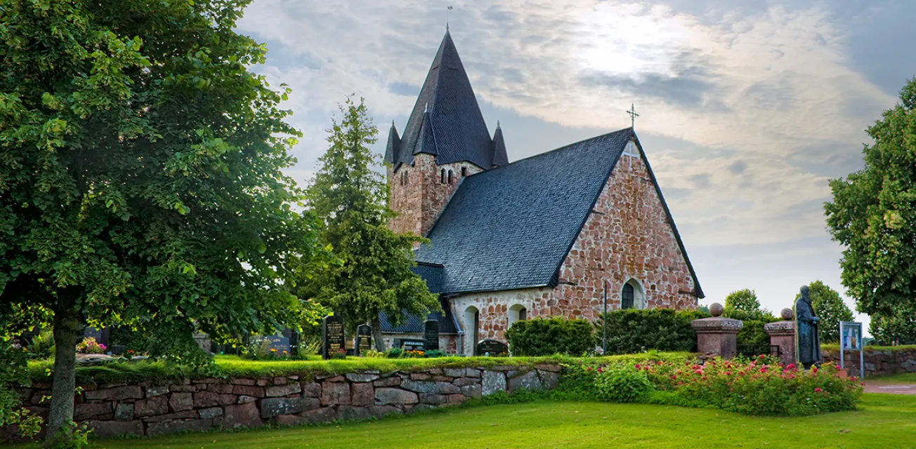 Finströms kyrka sommartid omgiven av lummiga träd.