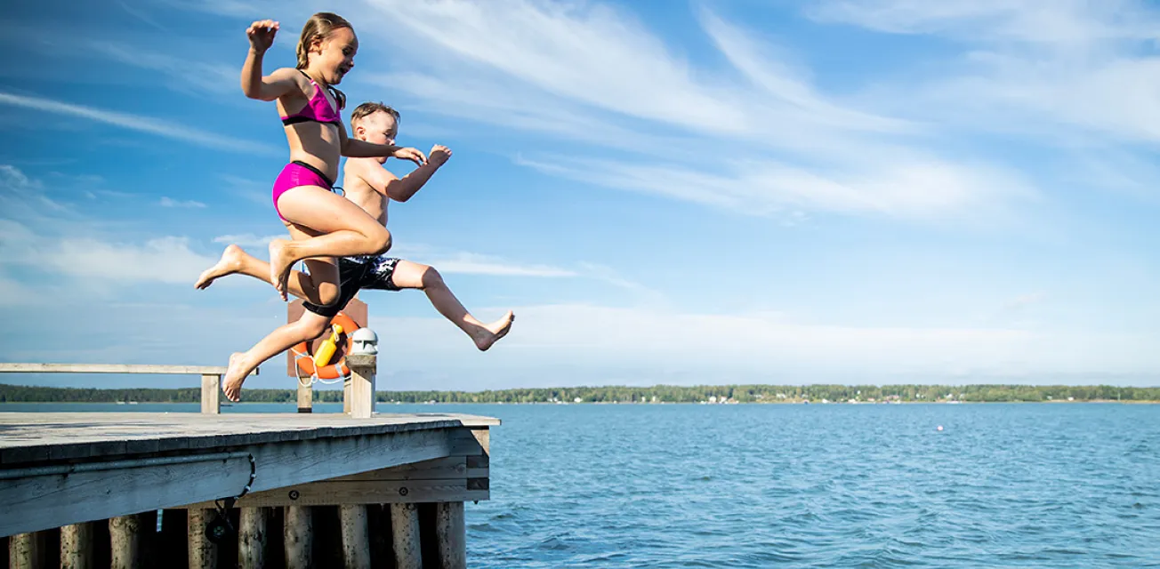 Barn som hoppar från bryggan vid badstranden Lilla Holmen i Mariehamn