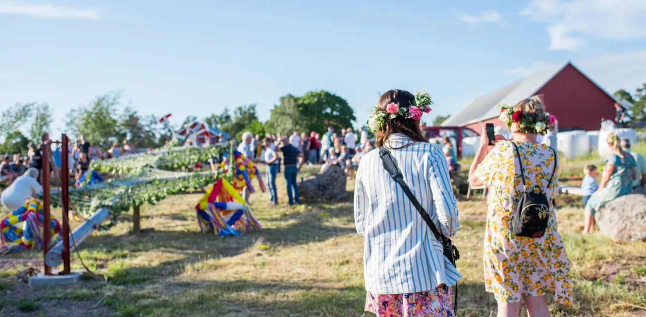 Kvinna fotograferar lövning av stången vid midsommarfirande på Bergö.