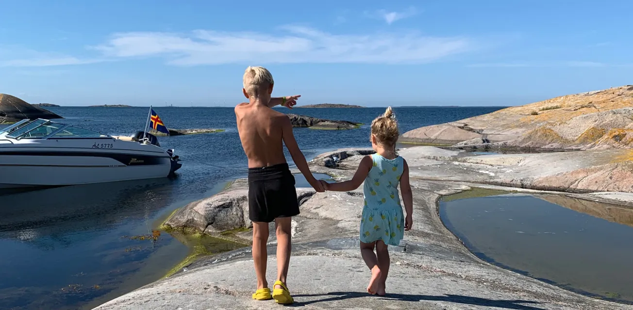 Pojke och flicka går hand i hand över klipporna på en ö i den åländska skärgården.