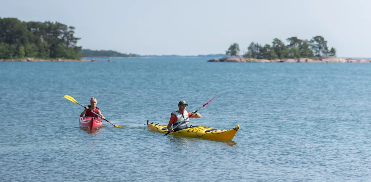 Två personer i varsin kajak som paddlar i Ålands skärgård.