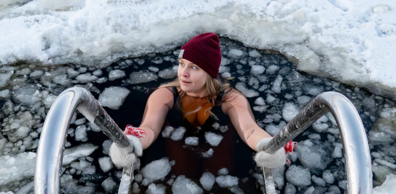 Kvinna vinterbadar i isig vak med badstege.