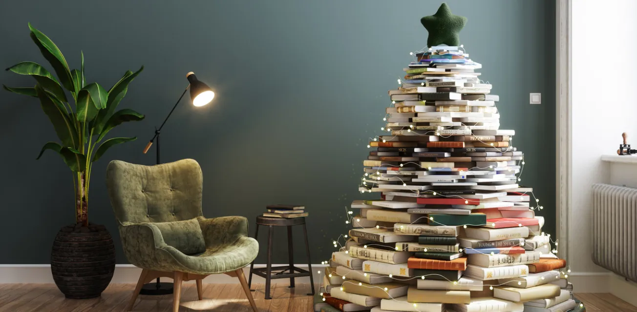 Julgran i form av böcker i ett vardagsrum med läsfotölj och lampa.