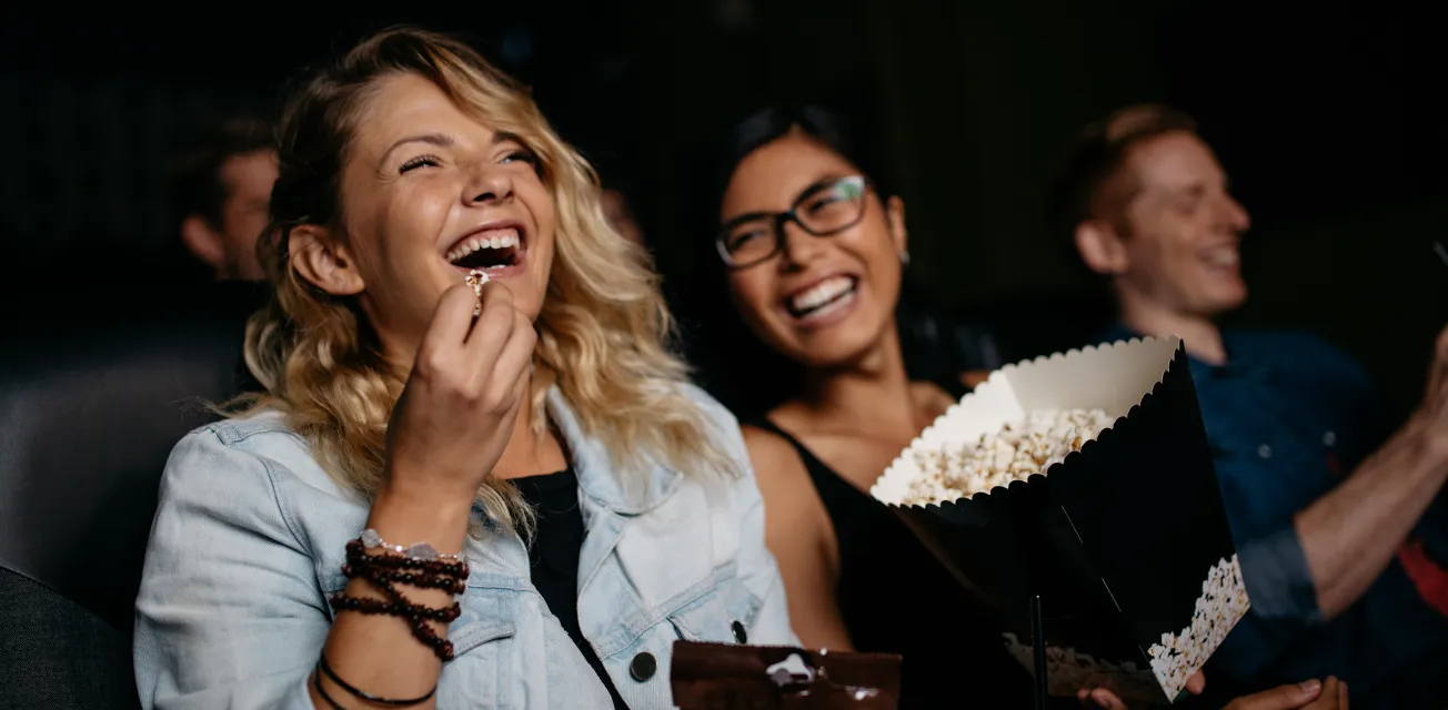 Unga kvinnor med popcorn skrattar på bio.