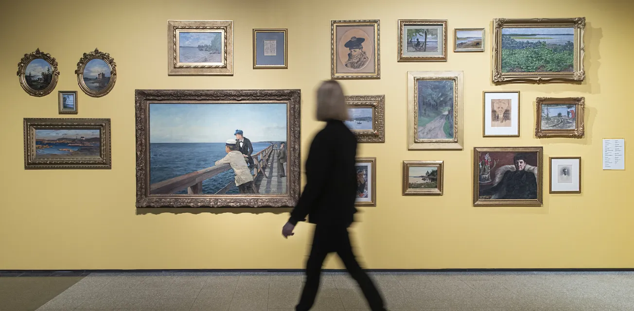 Kvinna tittar på tavlor i utställning vid Ålands konstmuseum.