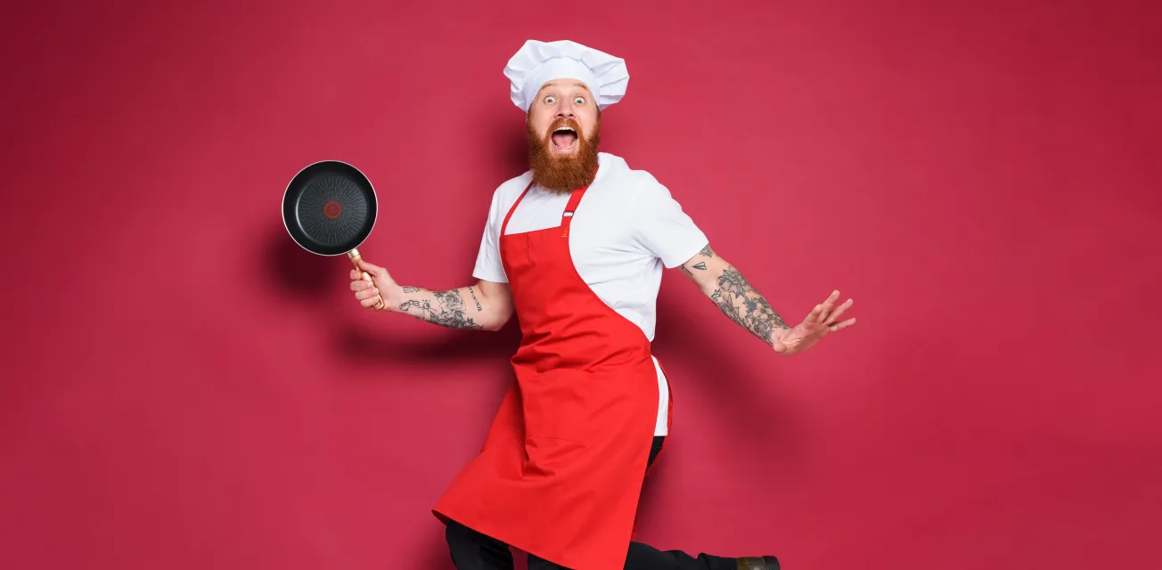 Kock med stekpanna och rött förkläde gör ett roligt hopp.