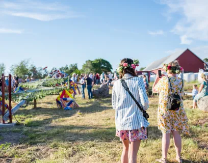 Kvinna fotograferar lövning av stången vid midsommarfirande på Bergö.