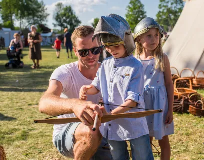 Barn med förälder spänner pilbåge på Vikingamarknaden i Kvarnbo.