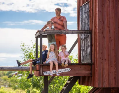 En man och fyra barn vid en röd kvarn på ett somrigt Åland.