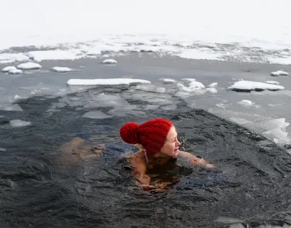 Kvinna med röd mössa vinterbadar i en isvak.