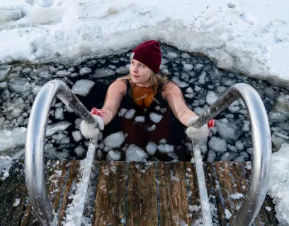 Kvinna vinterbadar i isig vak med badstege.