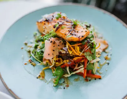 Gourmettallrik med grillad lax, inlagda och färska grönsaker och topping på en ljusblå tallrik.