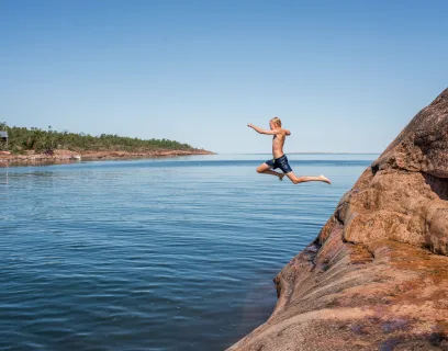 Pojke hoppar i vattnet från badklippa på Åland.