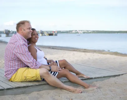 Par sitter på trägången vid Lilla holmens badstrand.