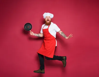 Kock med stekpanna och rött förkläde gör ett roligt hopp.