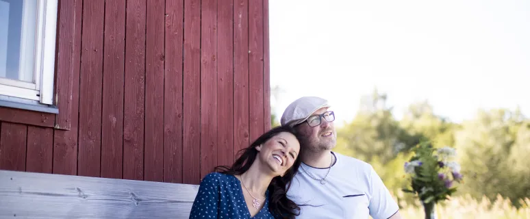 Par som sitter och fikar framför röd stuga.