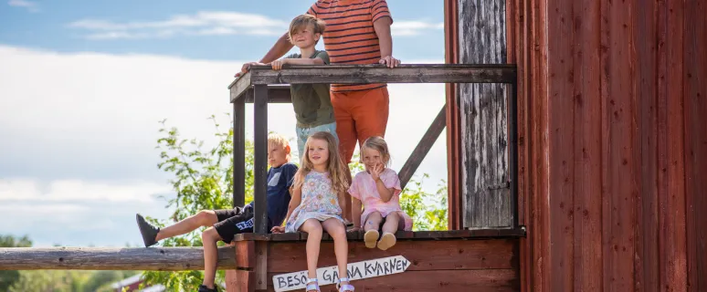 En man och fyra barn vid en röd kvarn på ett somrigt Åland.