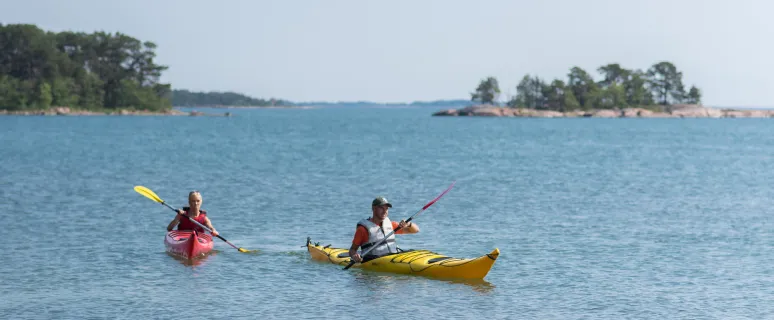 Två personer i varsin kajak som paddlar i Ålands skärgård.