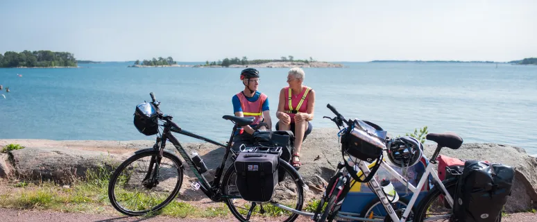 Cyklister på cykelsemester sitter och vilar på en klippa vid havet på Åland.