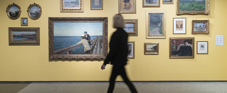 Kvinna tittar på tavlor i utställning vid Ålands konstmuseum.